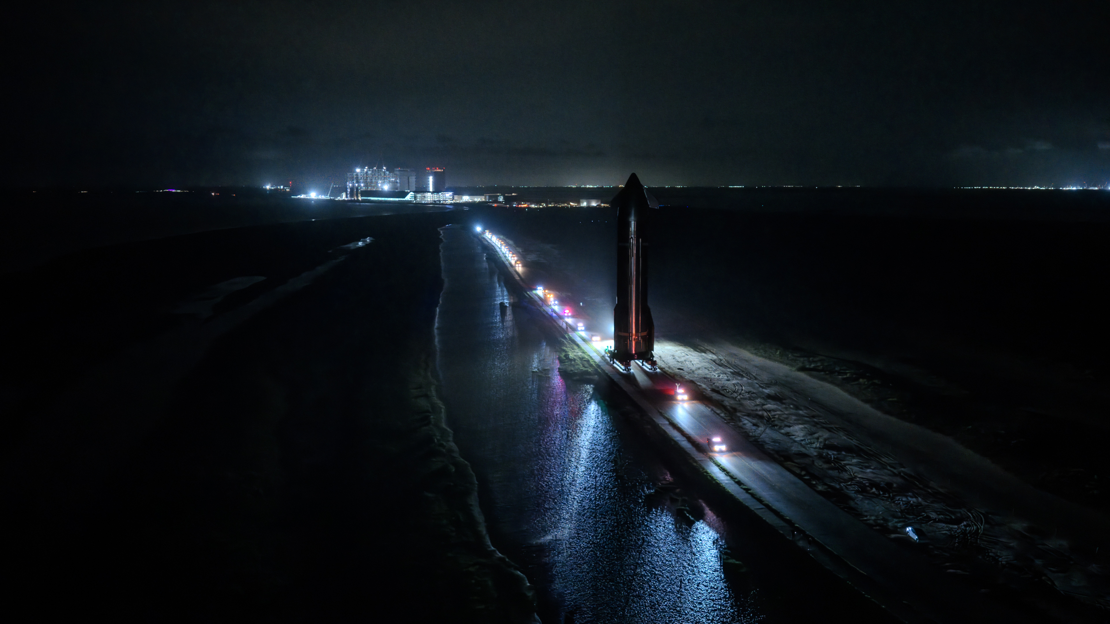 Nocturnal aerospace transporter moving along coastal highway under atmospheric lighting